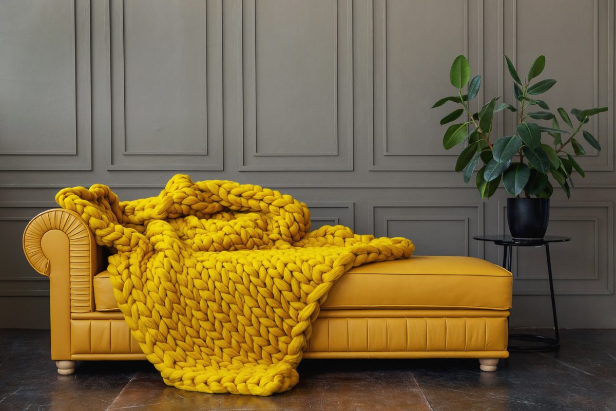 A yellow chunky knit blanket laid on a sofa