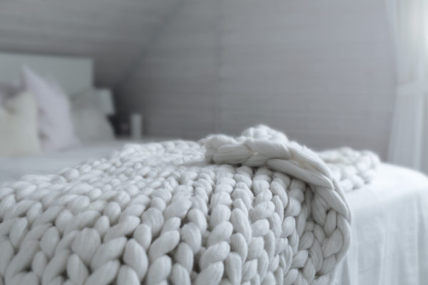 a natural white chunky knit bed runner on a white bed